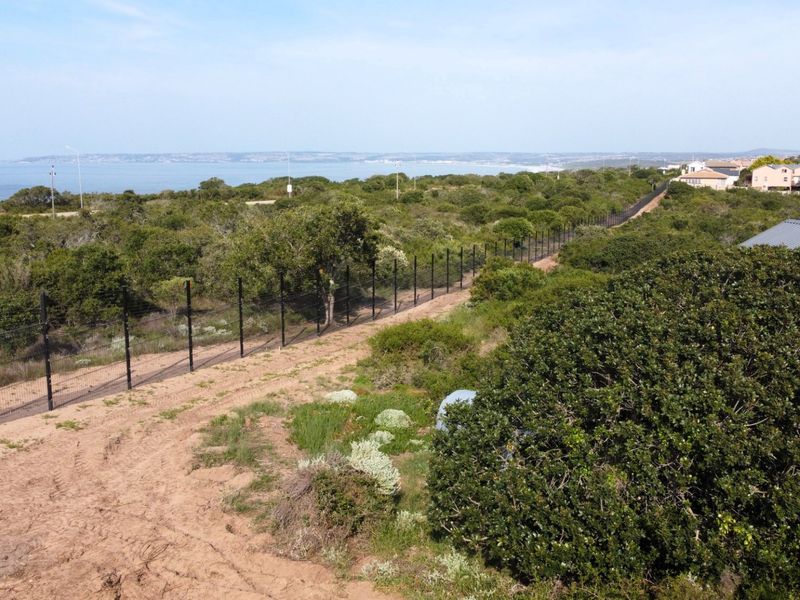 Aerial view of a vacant residential plot featuring perimeter fencing and natural coastal vegetation with distant ocean views.