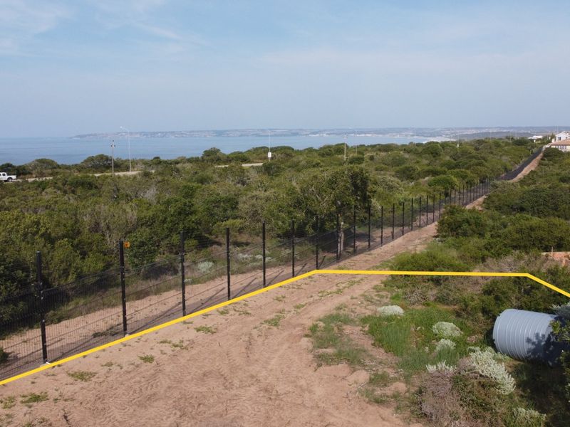 Aerial view of a vacant residential plot featuring perimeter fencing, a water tank, and scenic coastal views.