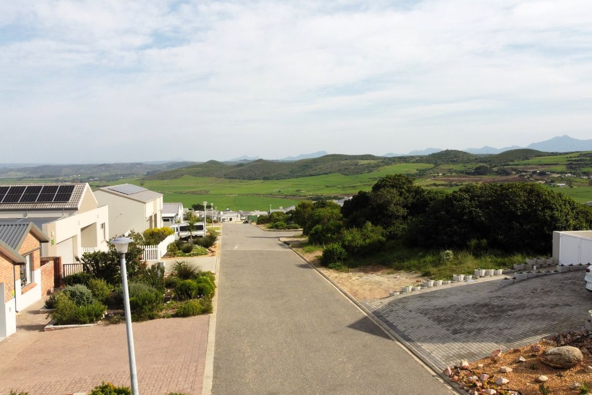 An elevated view overlooking a residential street with surrounding green hills and landscape in the distance.