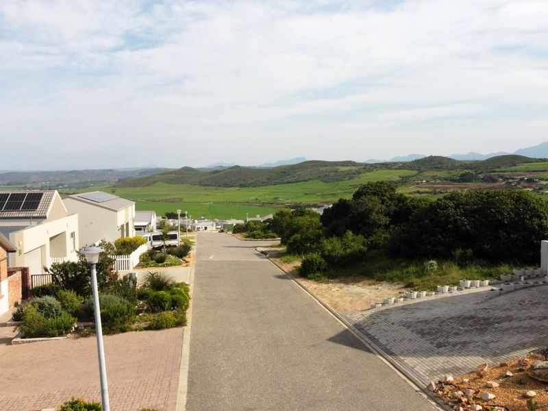 An elevated view overlooking a residential street with surrounding green hills and landscape in the distance.