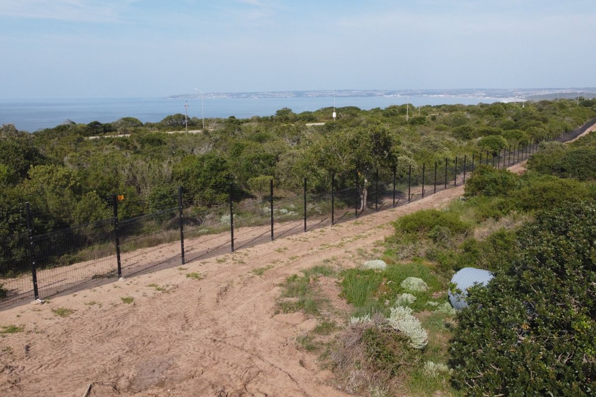 Aerial view of a vacant residential plot featuring perimeter fencing and natural coastal vegetation with ocean views in the background.