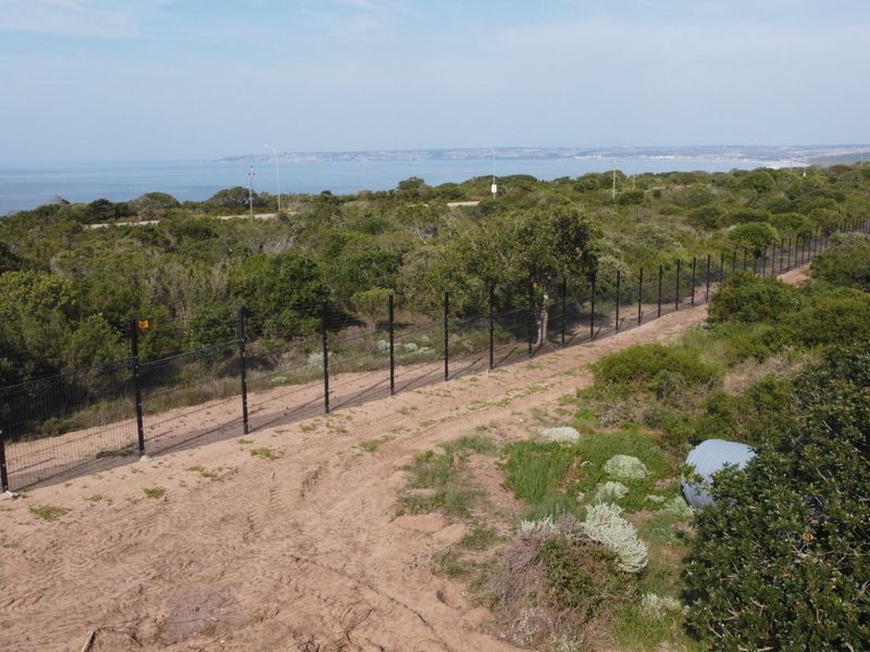 Aerial view of a vacant residential plot featuring perimeter fencing and natural coastal vegetation with ocean views in the background.