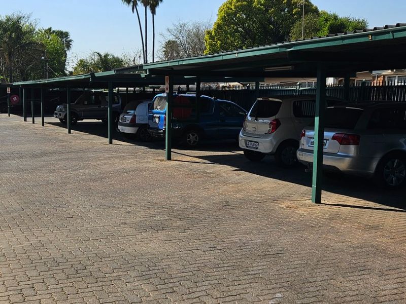 A communal covered parking area featuring a paved driveway and steel-framed shade structures for multiple vehicles.