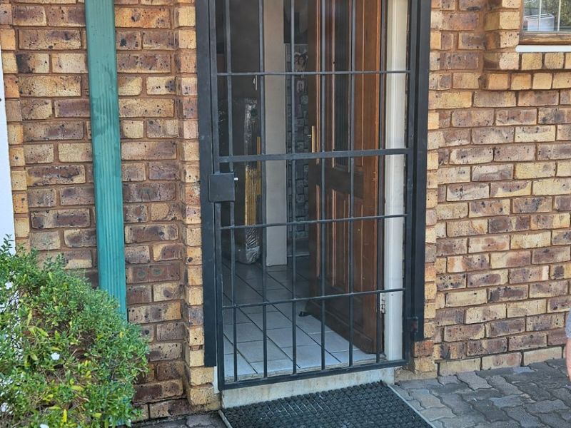 Exterior view of the townhouse entrance featuring a face brick facade, protective security gate, and a functional awning over the doorway.