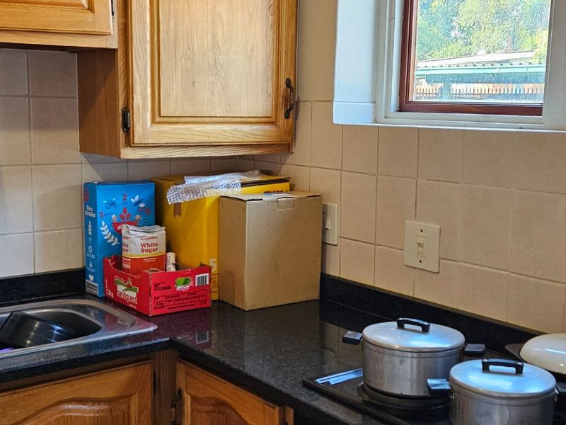 A functional kitchen featuring wooden cabinetry, black granite countertops, a built-in oven, and an electric hob with a tiled backsplash and flooring.