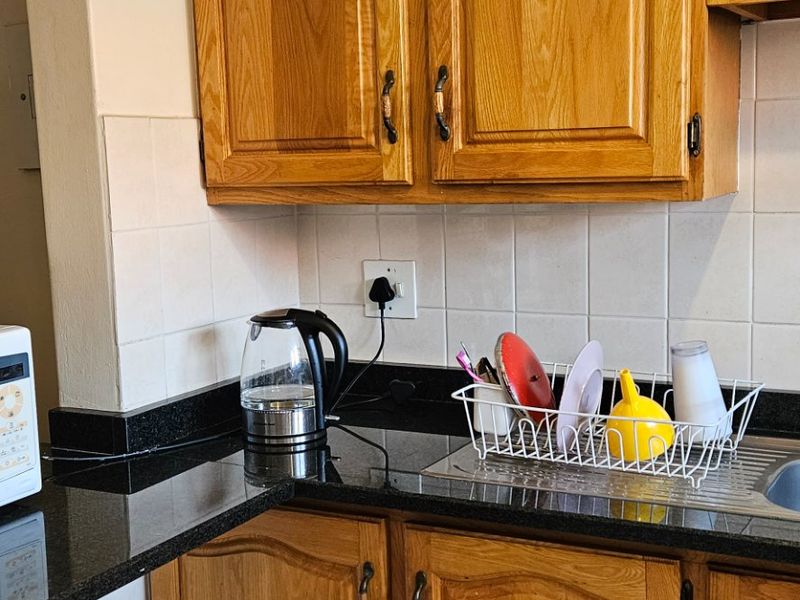 A functional kitchen area featuring traditional wooden cabinetry, dark granite countertops, and a tiled backsplash with a stainless steel sink.
