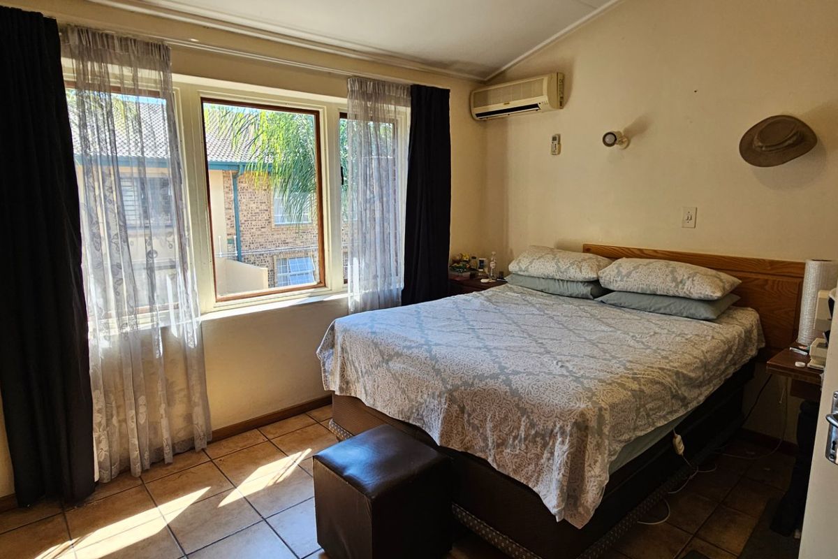 A functional bedroom featuring tiled flooring, a wall-mounted split-system air conditioner, and large windows allowing natural light.