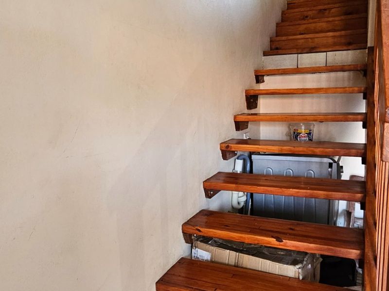 A wooden staircase with a matching handrail leading to an upper level, featuring tiled flooring and neutral wall finishes.