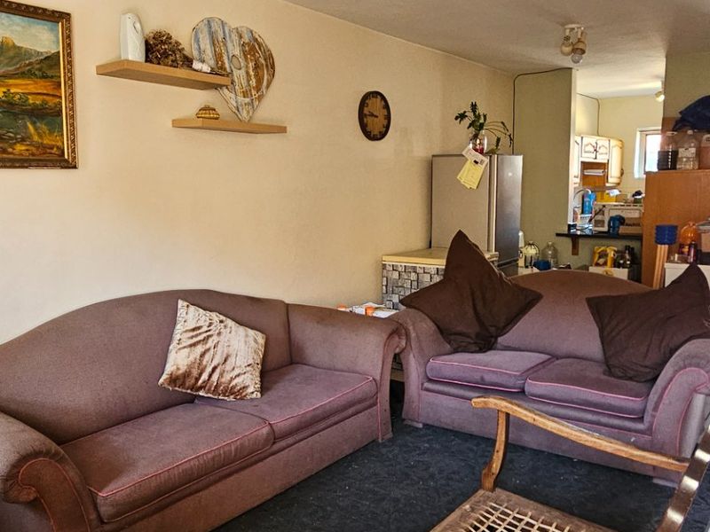 Open plan living area featuring a combination of tiled and carpeted flooring, wall-mounted shelving, and direct access to the kitchen space.