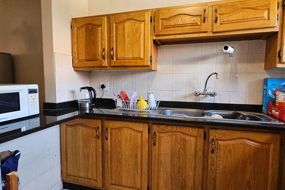 A functional kitchen featuring traditional oak-style cabinetry, dark granite countertops, and a double stainless steel sink with a tiled backsplash.