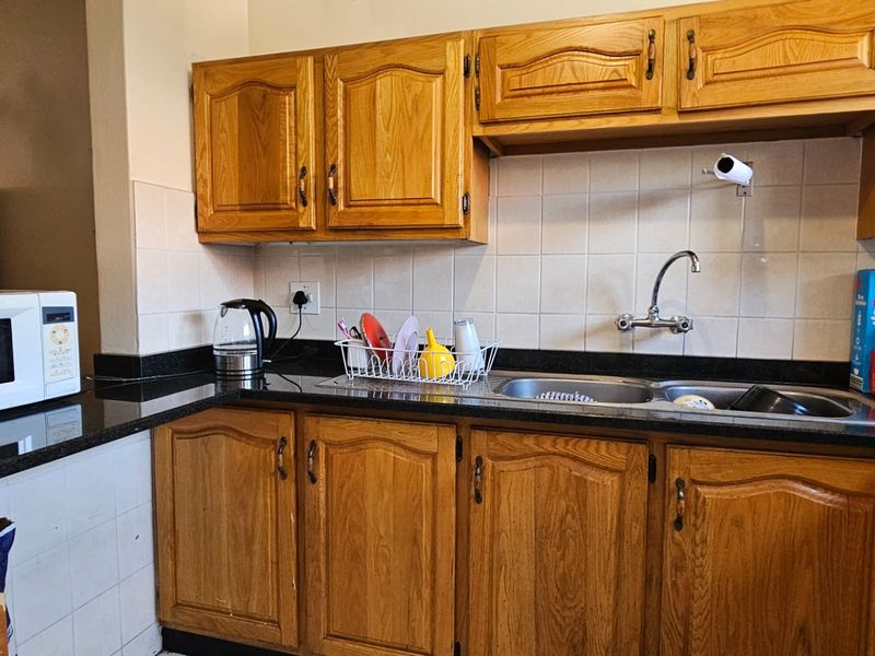 A functional kitchen featuring traditional oak-style cabinetry, dark granite countertops, and a double stainless steel sink with a tiled backsplash.
