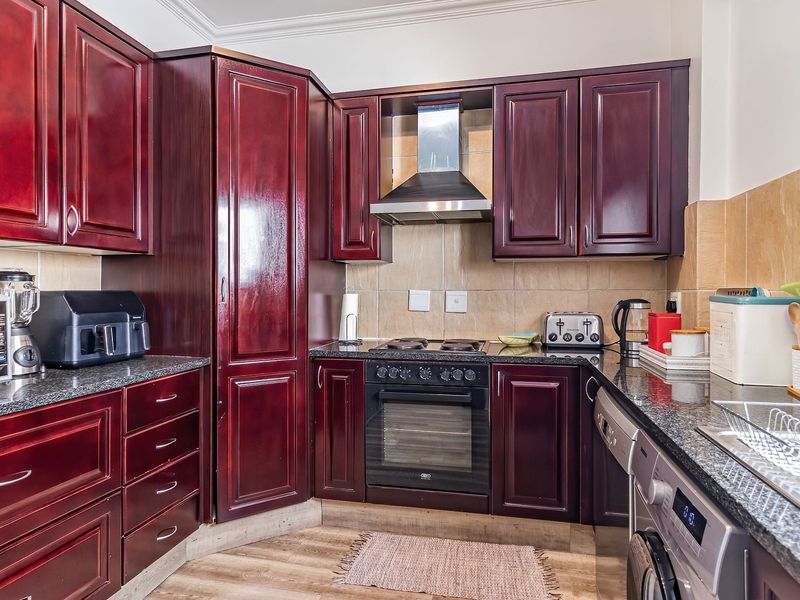 A functional kitchen featuring dark wood cabinetry, granite countertops, a built-in oven with extractor fan, and a tiled backsplash.