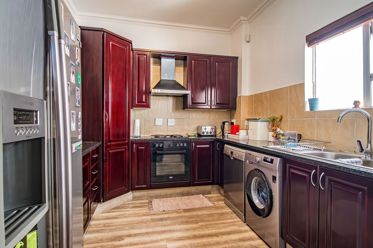 A functional kitchen featuring dark wood cabinetry, tiled backsplash, integrated oven and hob, and stainless steel sink with ample counter space.
