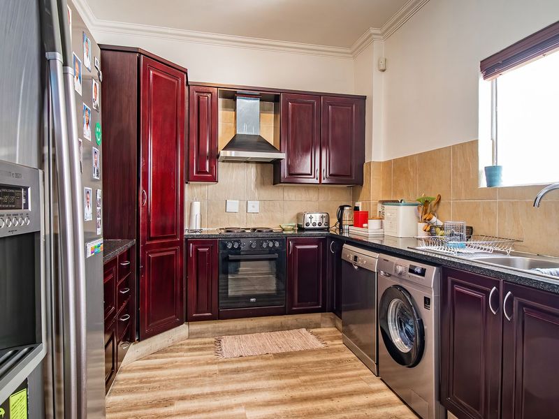 A functional kitchen featuring dark wood cabinetry, tiled backsplash, integrated oven and hob, and stainless steel sink with ample counter space.