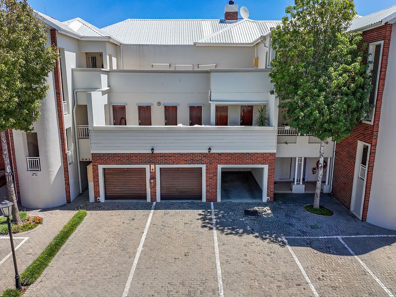 Front elevation of an apartment complex featuring multiple garage units, paved parking area, and upper-level balcony access.