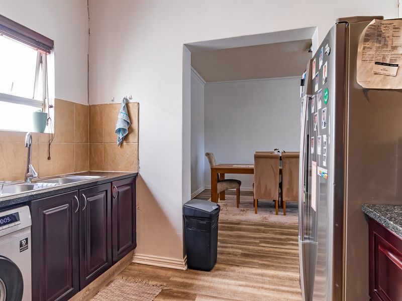 A functional kitchen featuring dark cabinetry, laminate countertops, and a tiled splashback, with an adjacent dining area visible through the doorway.