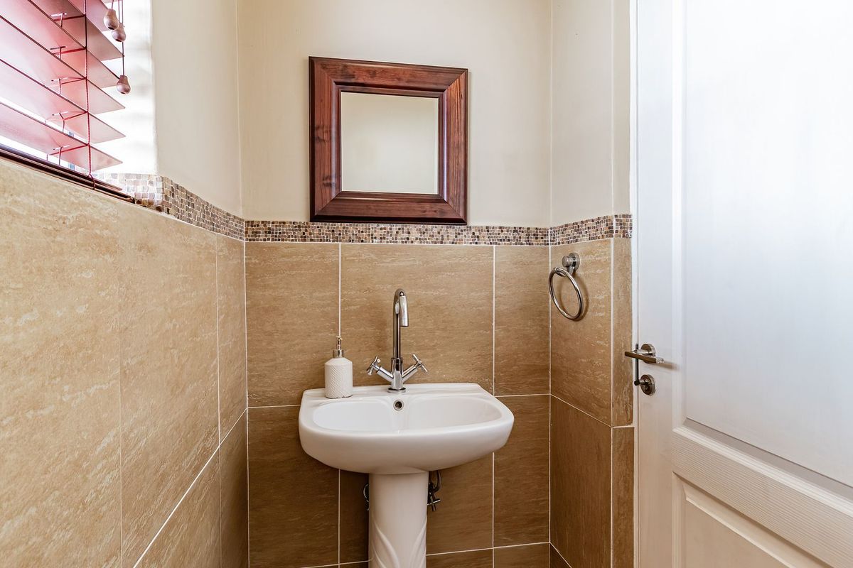 A compact guest bathroom featuring a pedestal basin, chrome mixer tap, and neutral wall tiling with a decorative mosaic border.
