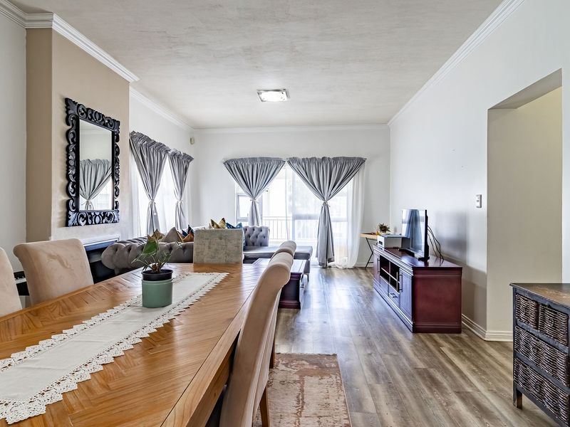 Spacious open-plan living and dining area featuring modern laminate flooring, crown molding, and large sliding glass doors providing natural light.