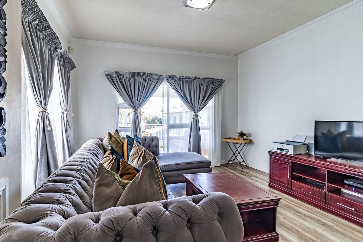 A well-lit living room featuring laminate flooring, crown molding, and a sliding glass door providing access to an outdoor area.