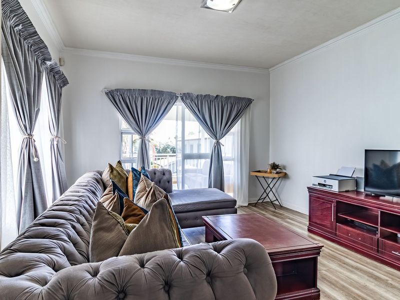 A well-lit living room featuring laminate flooring, crown molding, and a sliding glass door providing access to an outdoor area.
