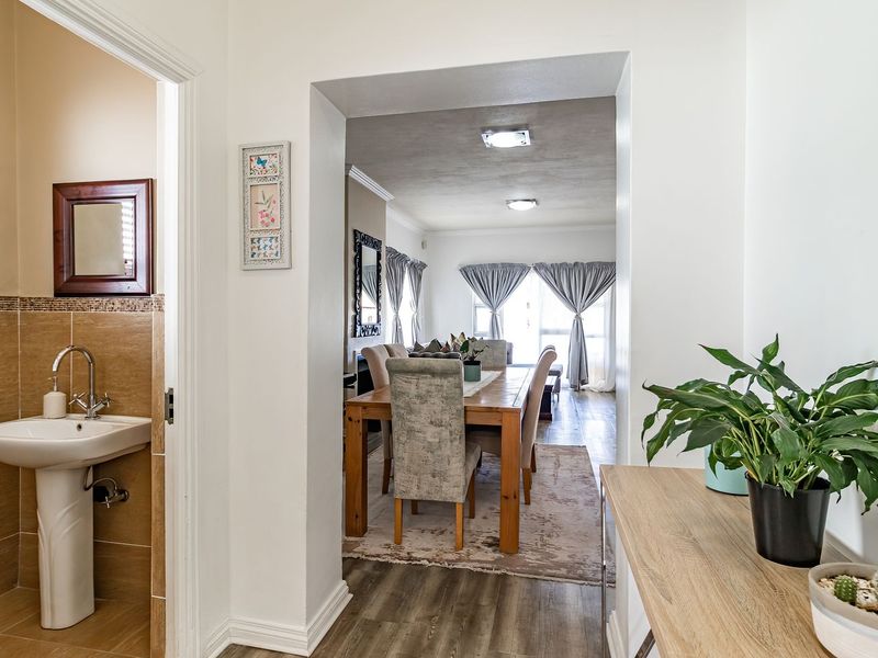A bright hallway entrance featuring a guest pedestal basin with tiled splashback, leading into an open-plan dining and living area with laminate flooring.