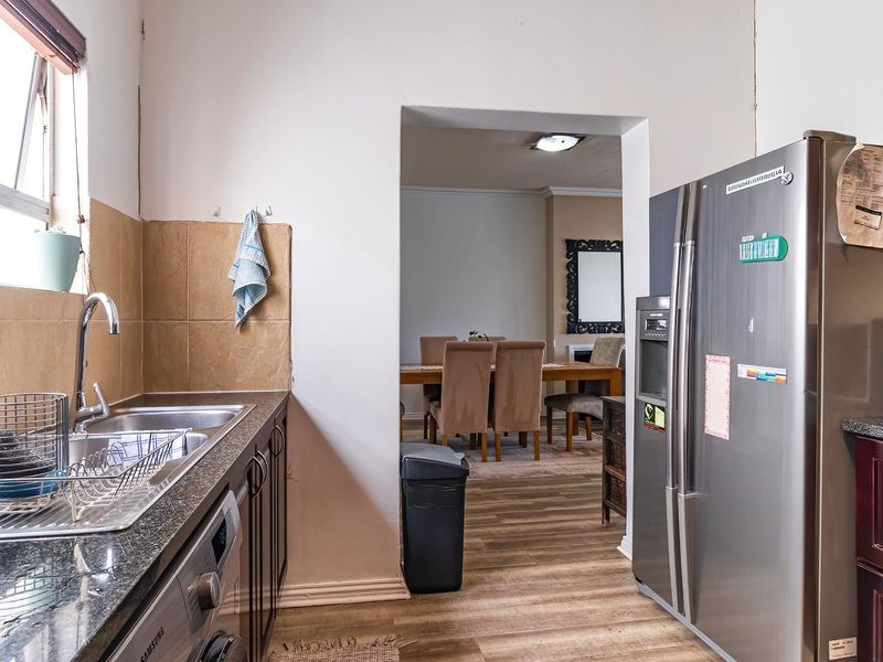 A functional kitchen featuring dark wood cabinetry, granite countertops, and a stainless steel sink, with a view through to the adjacent dining area.