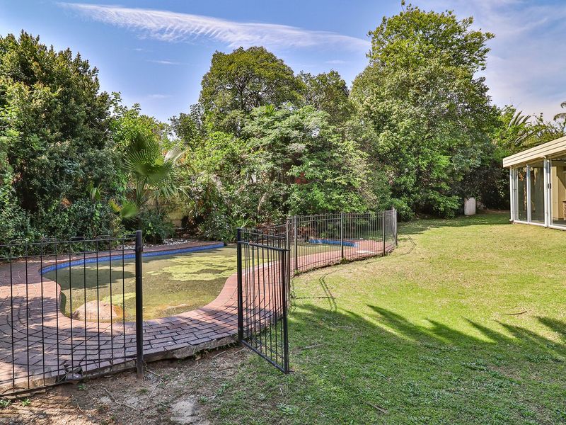 Rear garden area featuring a swimming pool with metal safety fencing, brick paving, and access to the main house via sliding glass doors.