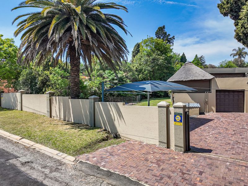 Front view of the property featuring a paved driveway, perimeter wall, shade sail parking, and a garage with a thatched roof section.