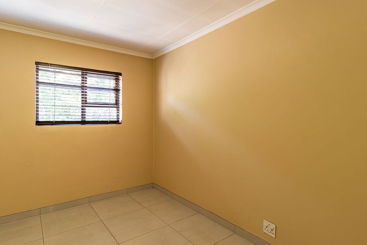 A clean, empty bedroom featuring neutral wall paint, tiled flooring, and a window fitted with venetian blinds.