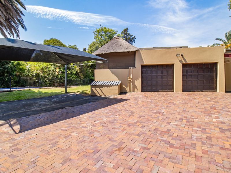 A spacious paved driveway leading to a double garage, featuring a shade sail and a small thatch-roofed outdoor structure.