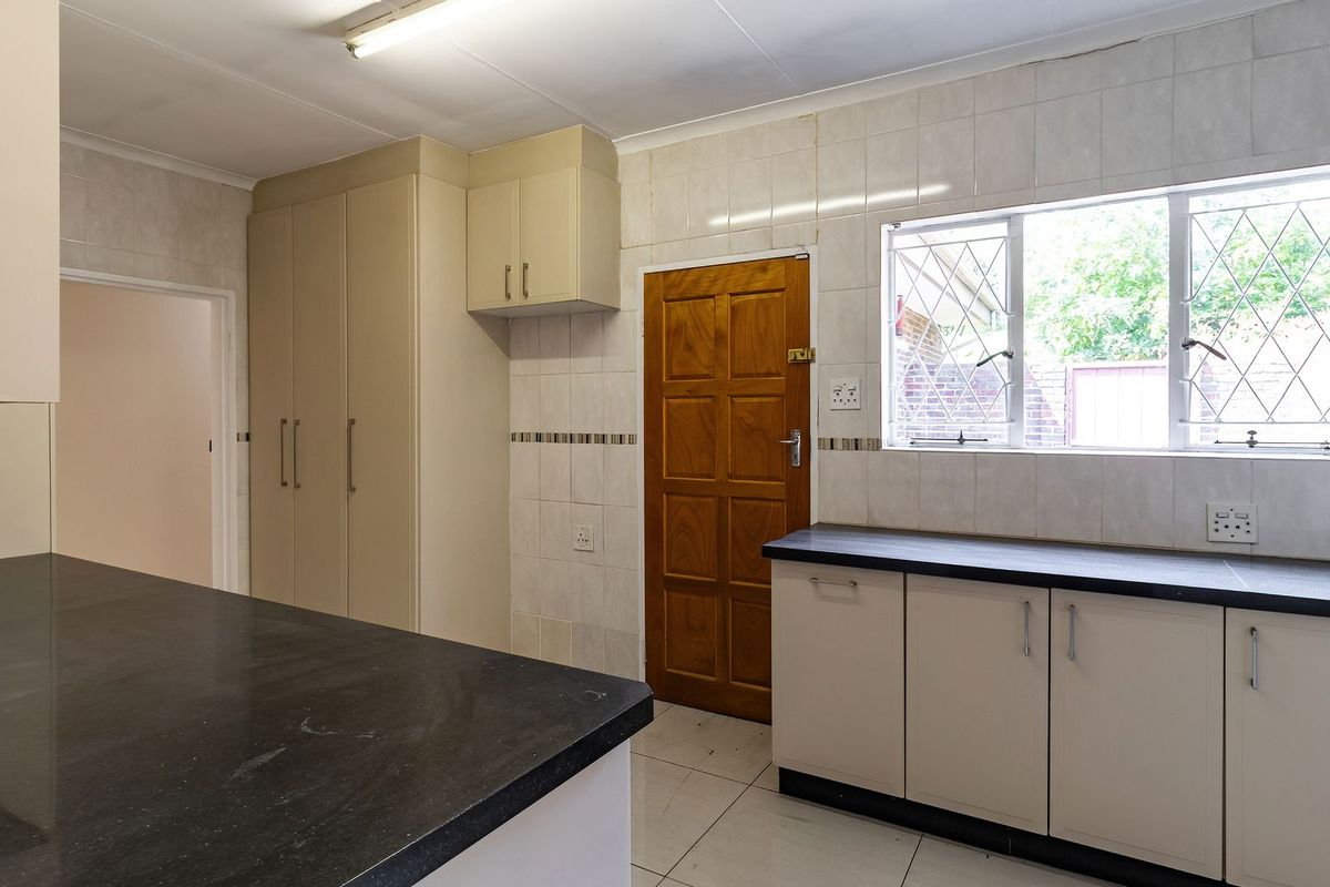 A functional kitchen featuring built-in cabinetry, dark laminate countertops, tiled backsplash, and tiled flooring, offering a clean and practical workspace.
