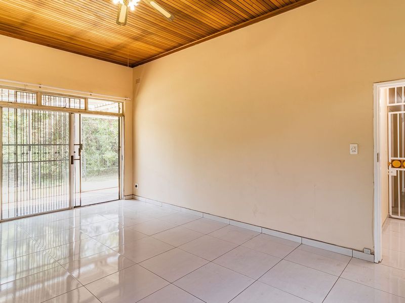 An empty living room featuring tiled flooring, a timber ceiling, and a sliding glass door with security gate access to the exterior.
