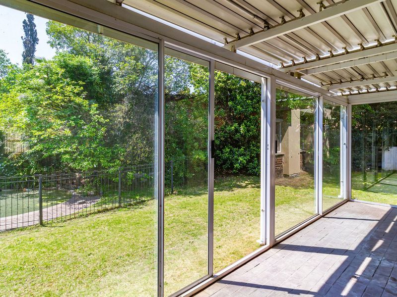 A covered patio area featuring paved flooring and large sliding glass doors that provide direct access to the rear garden and pool area.