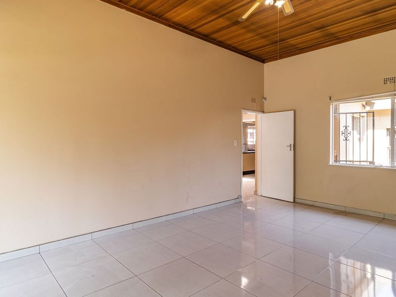 An empty living room featuring ceramic floor tiles, a timber ceiling, and security bars on the windows.