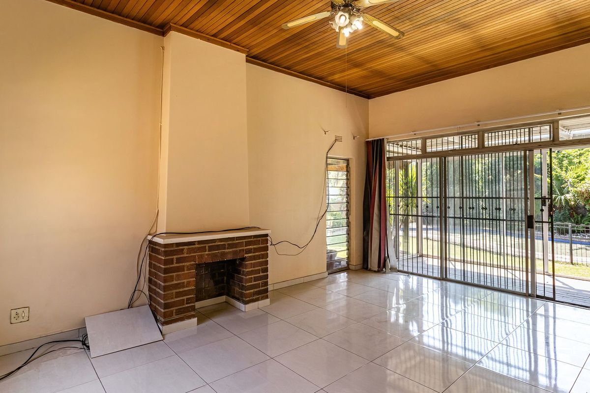Spacious living room featuring a brick fireplace, timber ceiling, and large sliding glass doors leading to the garden, offering a bright and open layout.