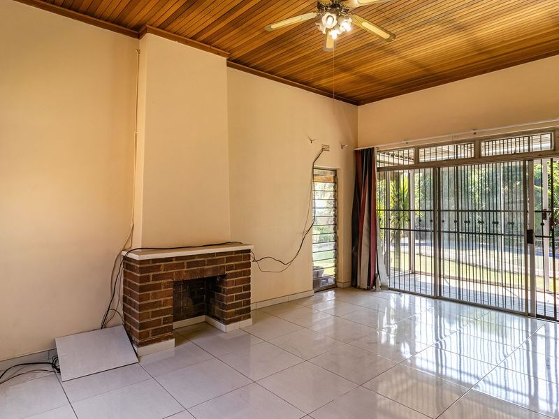 Spacious living room featuring a brick fireplace, timber ceiling, and large sliding glass doors leading to the garden, offering a bright and open layout.