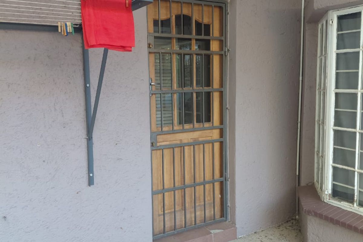 A covered patio area featuring a timber door with a security gate, a bay window, and a wall-mounted drying rack.