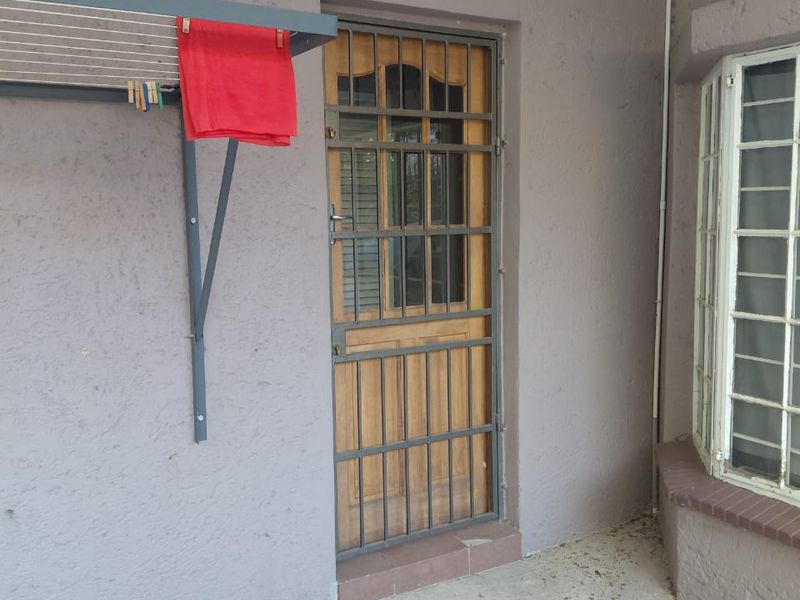 A covered patio area featuring a timber door with a security gate, a bay window, and a wall-mounted drying rack.