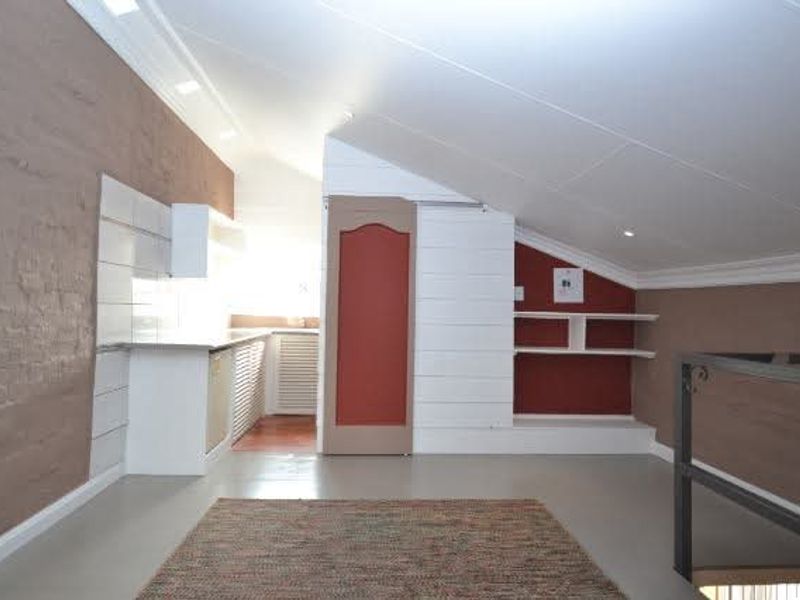 An open-plan attic space featuring sloped ceilings, recessed lighting, built-in shelving, and a compact kitchen area with neutral finishes.