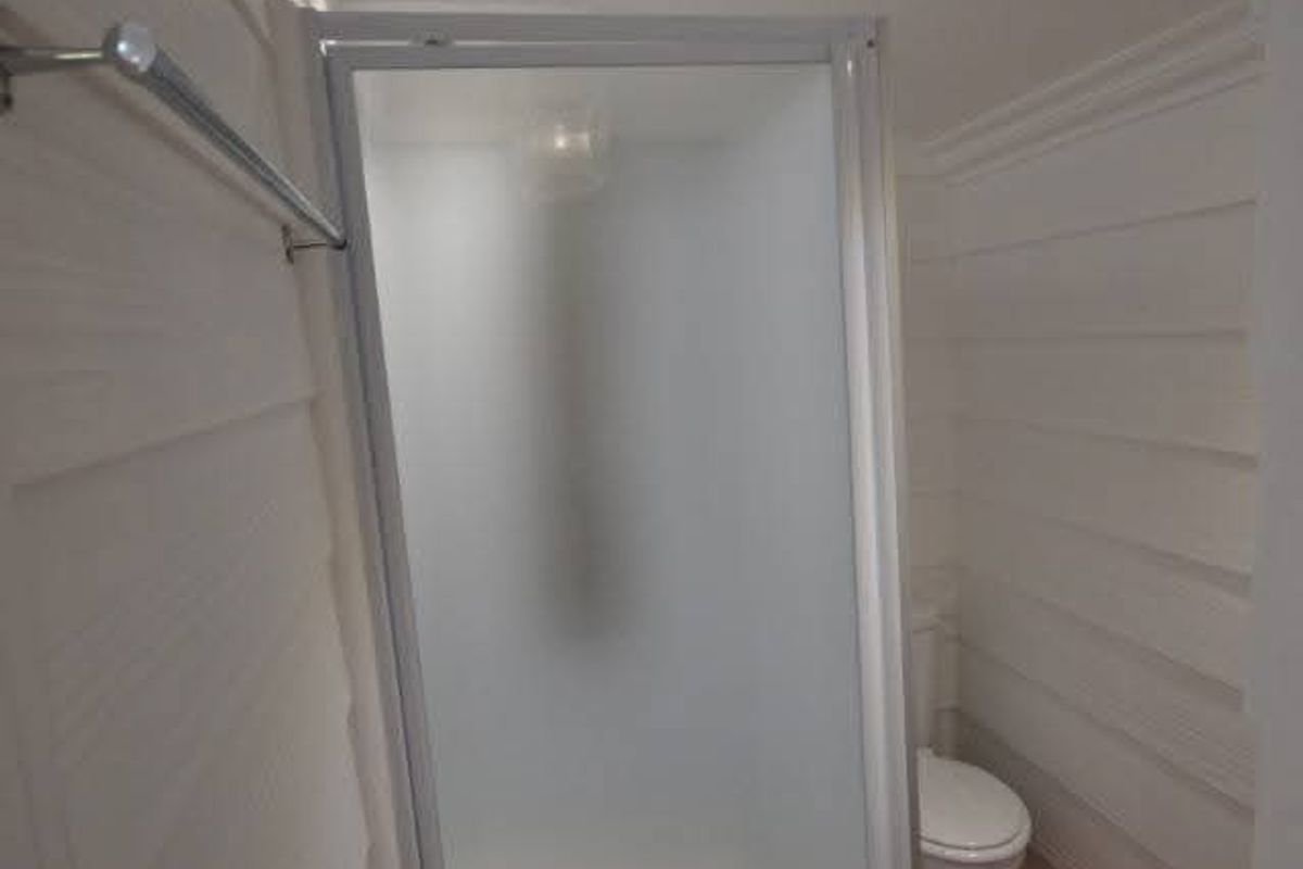 A clean, modern bathroom featuring a glass shower enclosure, a toilet, recessed lighting, and warm timber flooring.