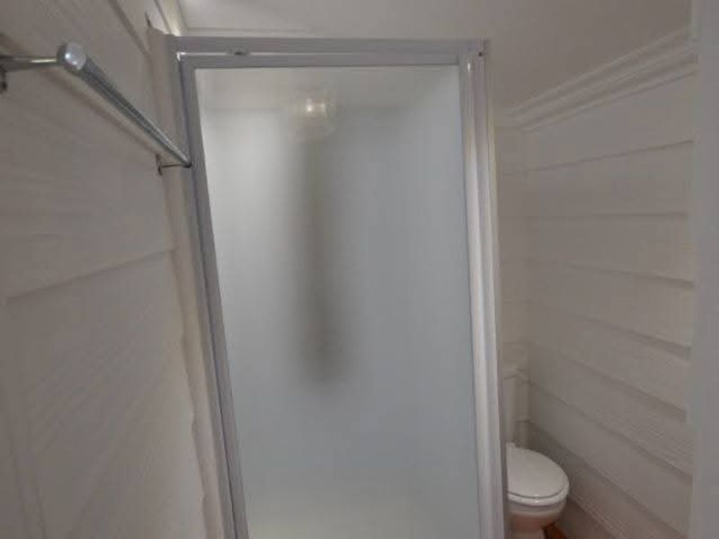 A clean, modern bathroom featuring a glass shower enclosure, a toilet, recessed lighting, and warm timber flooring.