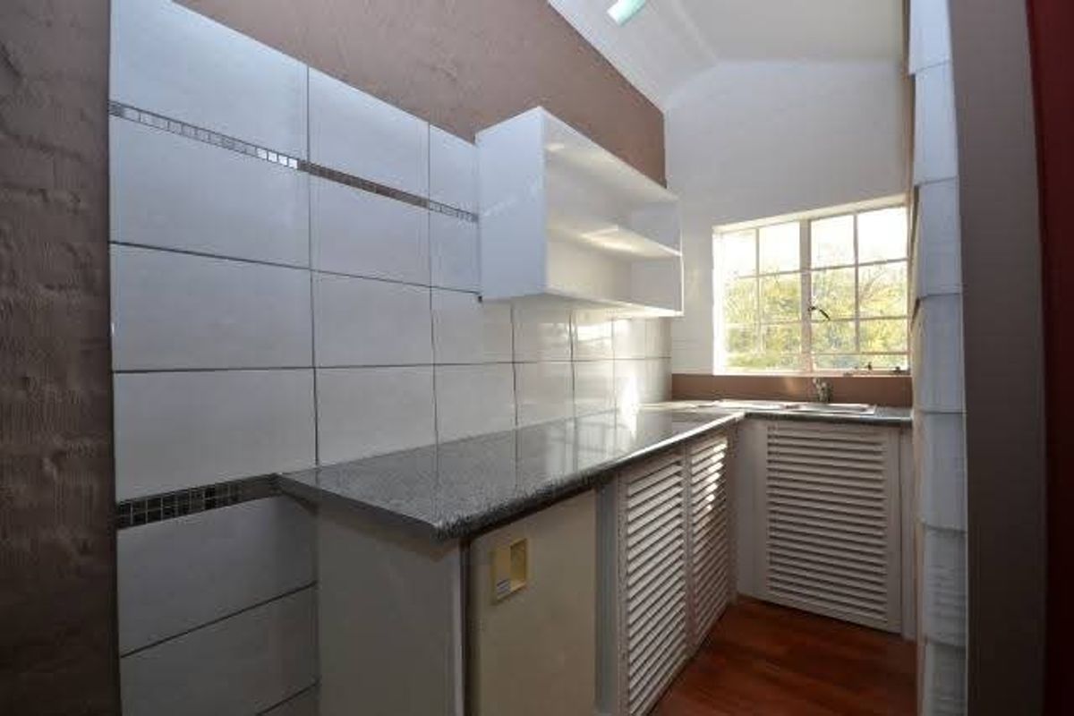 A functional scullery area featuring granite countertops, tiled splashbacks, louvered cabinetry, and a stainless steel sink with natural light.