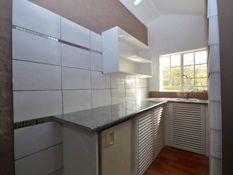 A functional scullery area featuring granite countertops, tiled splashbacks, louvered cabinetry, and a stainless steel sink with natural light.