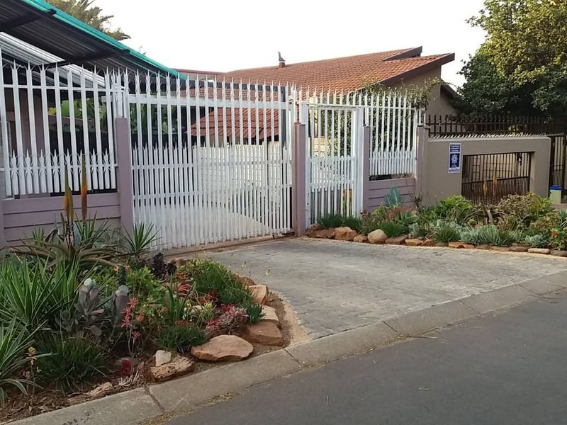 Front exterior view of the property featuring a paved driveway, secure white metal fencing, and well-maintained landscaped garden beds.