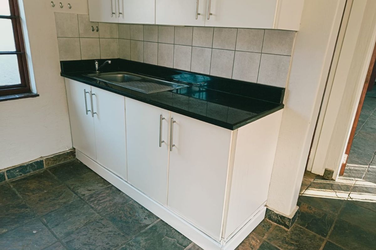 A compact kitchen area featuring white cabinetry, dark stone countertops, a stainless steel sink, and durable slate flooring.