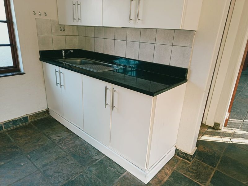 A compact kitchen area featuring white cabinetry, dark stone countertops, a stainless steel sink, and durable slate flooring.