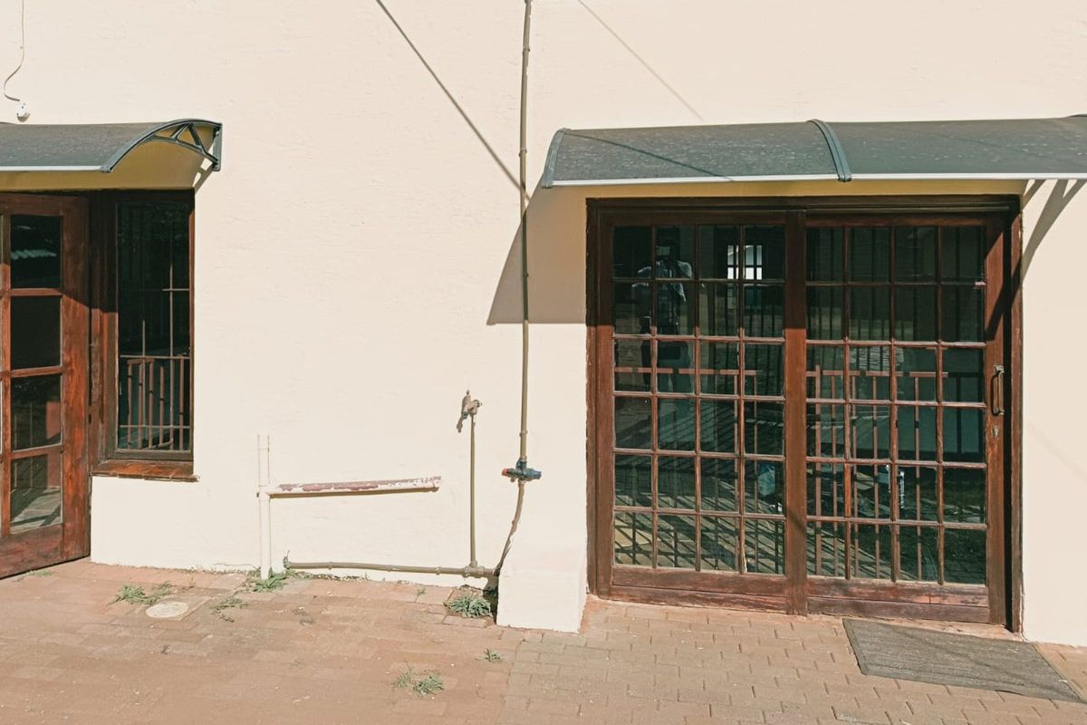 Rear exterior view featuring timber-framed glass doors, protective awnings, and a paved patio area with external plumbing fixtures.