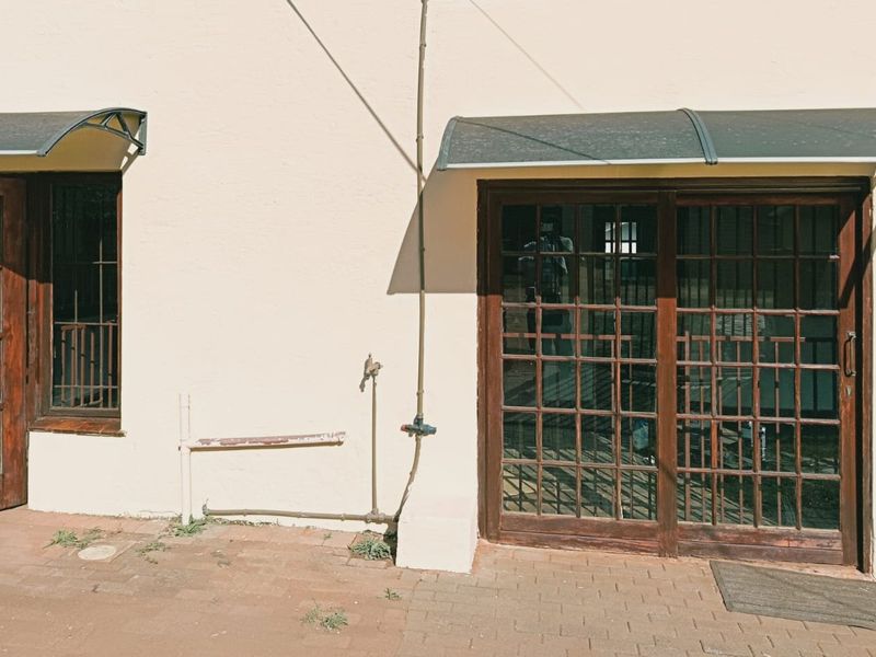 Rear exterior view featuring timber-framed glass doors, protective awnings, and a paved patio area with external plumbing fixtures.