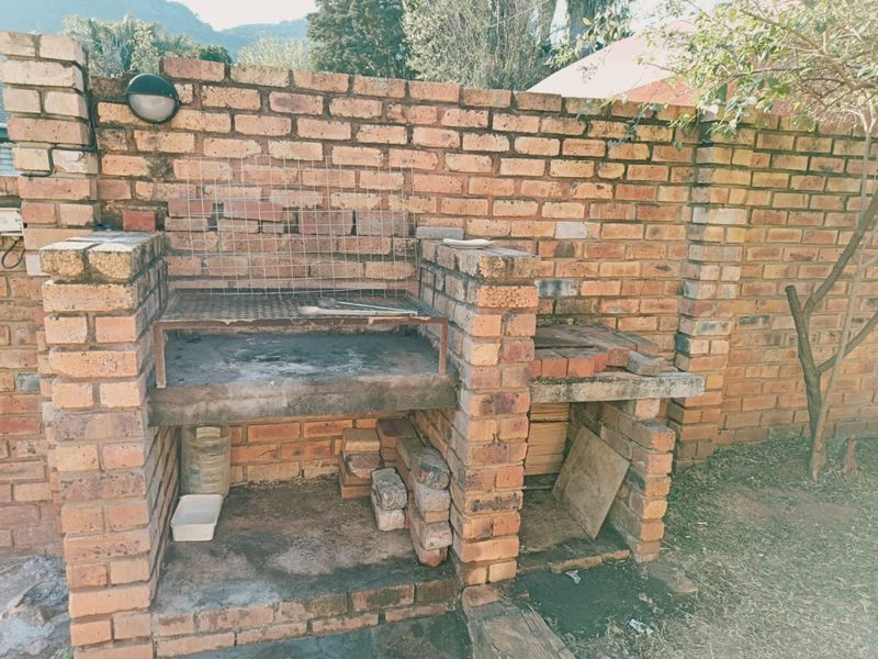 A rustic outdoor brick braai area featuring a built-in grill and integrated storage space, set against a brick boundary wall.