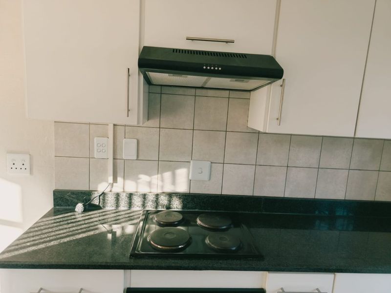 A functional kitchen area featuring white cabinetry, a dark stone countertop, tiled backsplash, and a built-in electric hob with an overhead extractor fan.